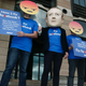 A protester wearing a mask of Facebook founder Mark Zuckerberg, in between men wearing angry face emoji masks. London, 2018.